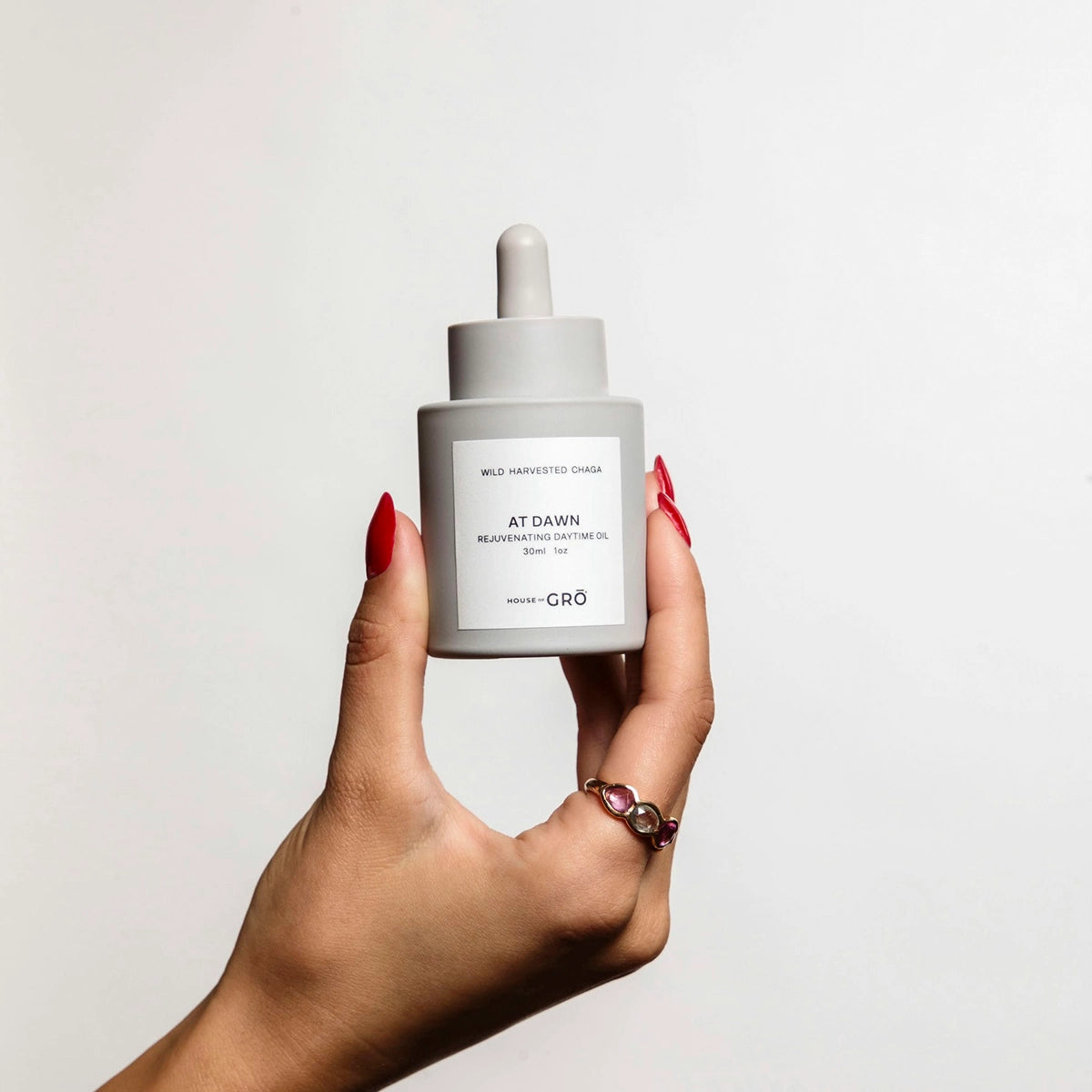 Hand holding the House of GRŌ At Dawn Rejuvenating Daytime Oil bottle to show its actual size and packaging design.