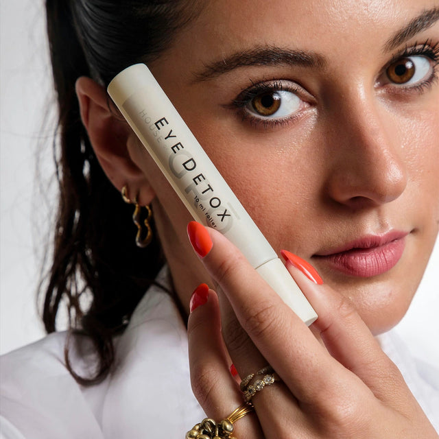 Close-up of a woman holding the House of GRŌ Eye Detox Brightening Oil next to her face.