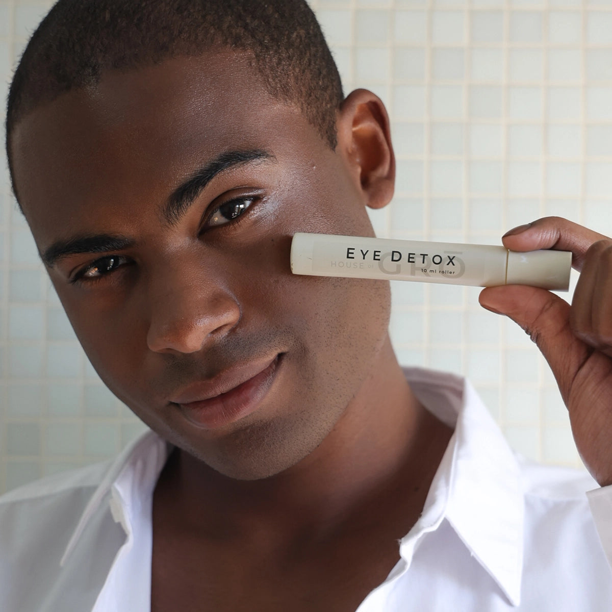 Man holding the House of GRŌ Eye Detox Brightening Oil near his cheek, highlighting natural men's skincare.