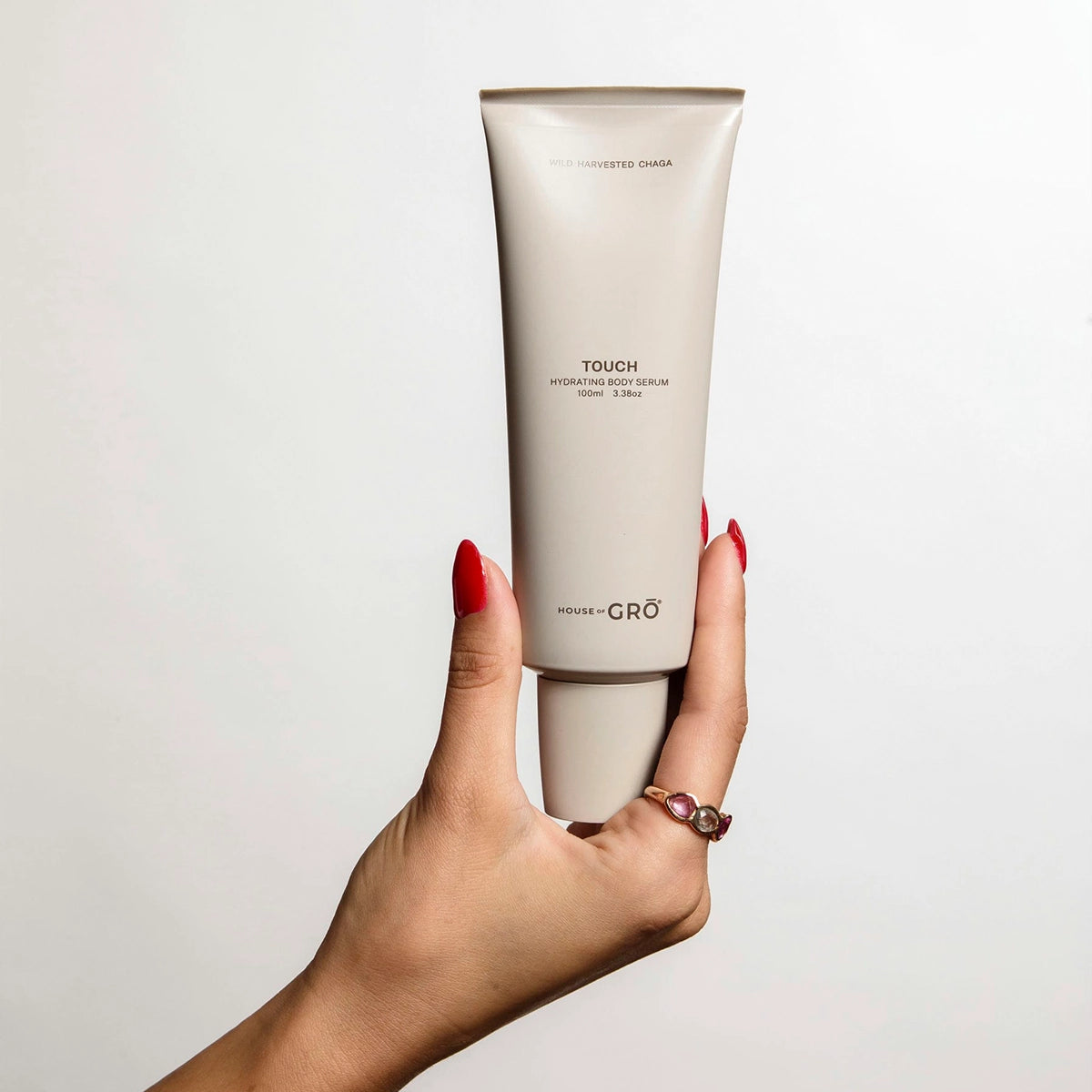 Hand holding the House of GRŌ Touch Hydrating Body Serum tube, displaying its actual size and minimalist packaging.