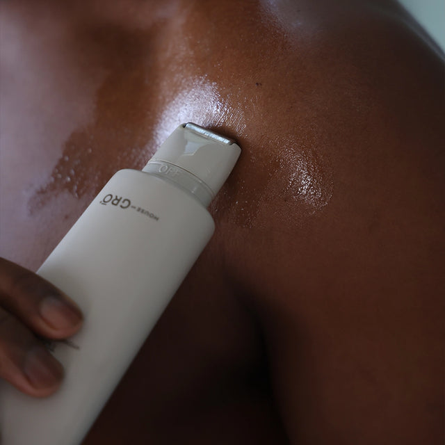 Close-up of a man applying the House of GRŌ Touch Hydrating Body Serum to his shoulder, highlighting its use for men's body care.